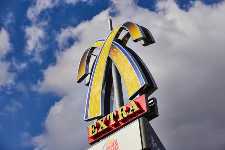 A towering mcdonald's sign with a golden arch against a cloudy blue sky, featuring a red board labeled "extra.