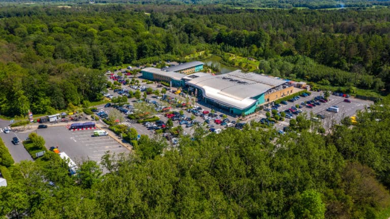 Aerial view of a busy parking lot at a motorway service area surrounded by greenery.