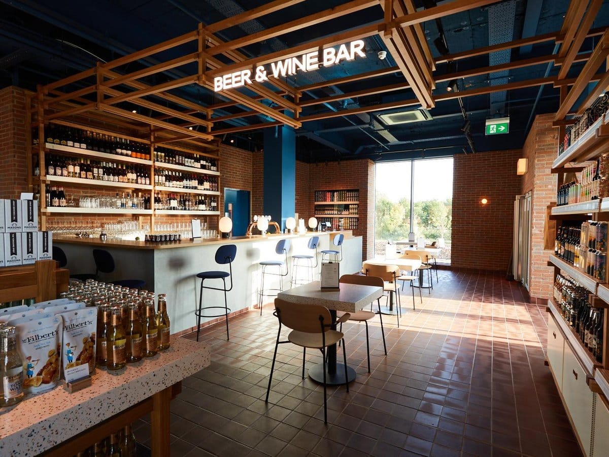 Modern bar interior with brick walls, a wooden ceiling, and shelves stocked with Drik bottles.