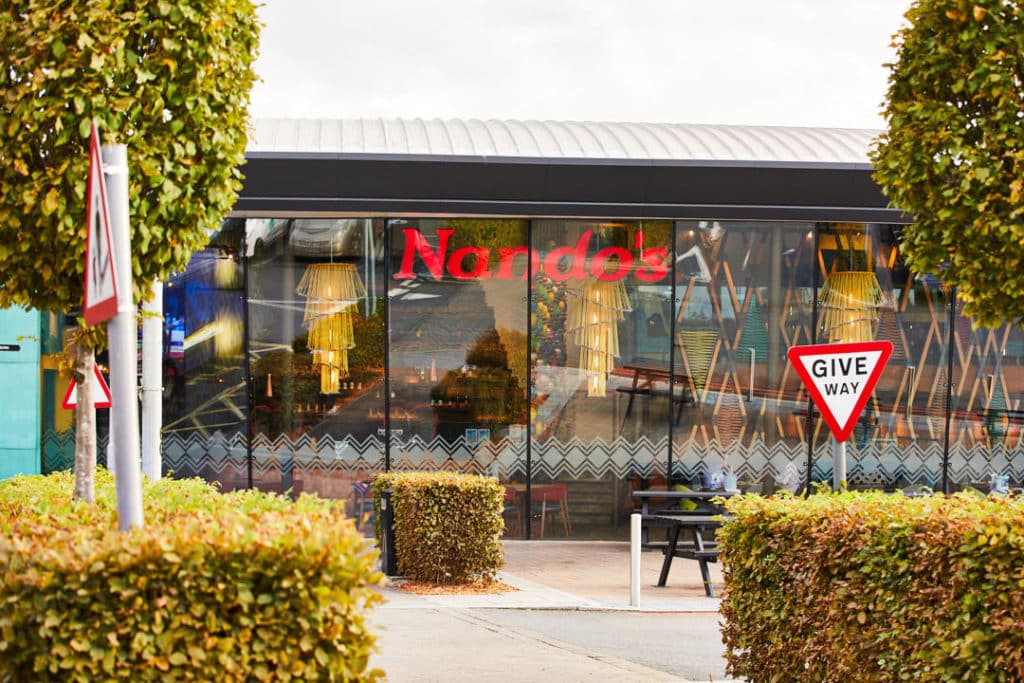 Exterior view of a nando's restaurant with landscaped bushes and traffic signs.