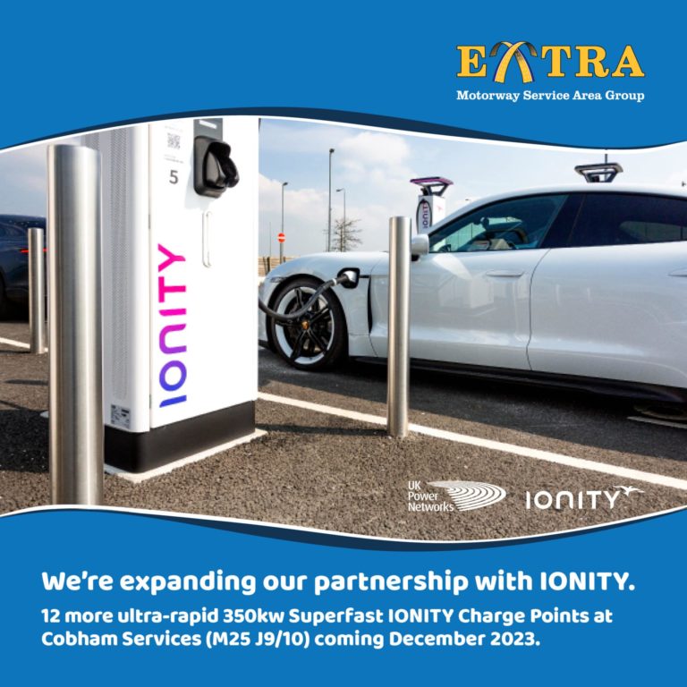 Electric vehicle charging station with a white car plugged in, advertising the expansion of charging points at a motorway service area.