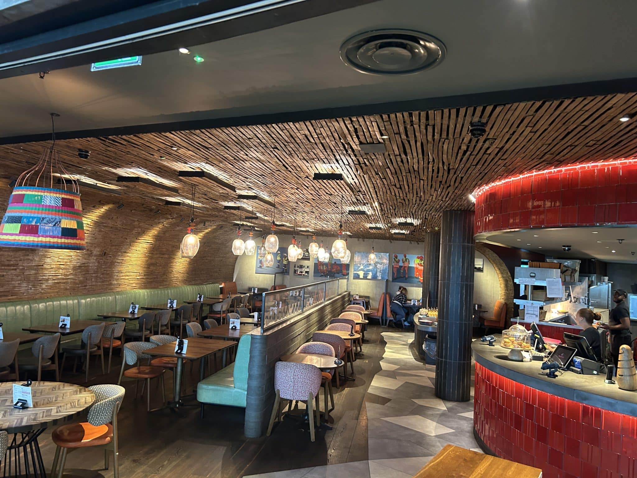 Modern restaurant interior with eclectic décor, featuring a bar area, dining tables, colorful lighting fixtures, and extra services including EV chargers.