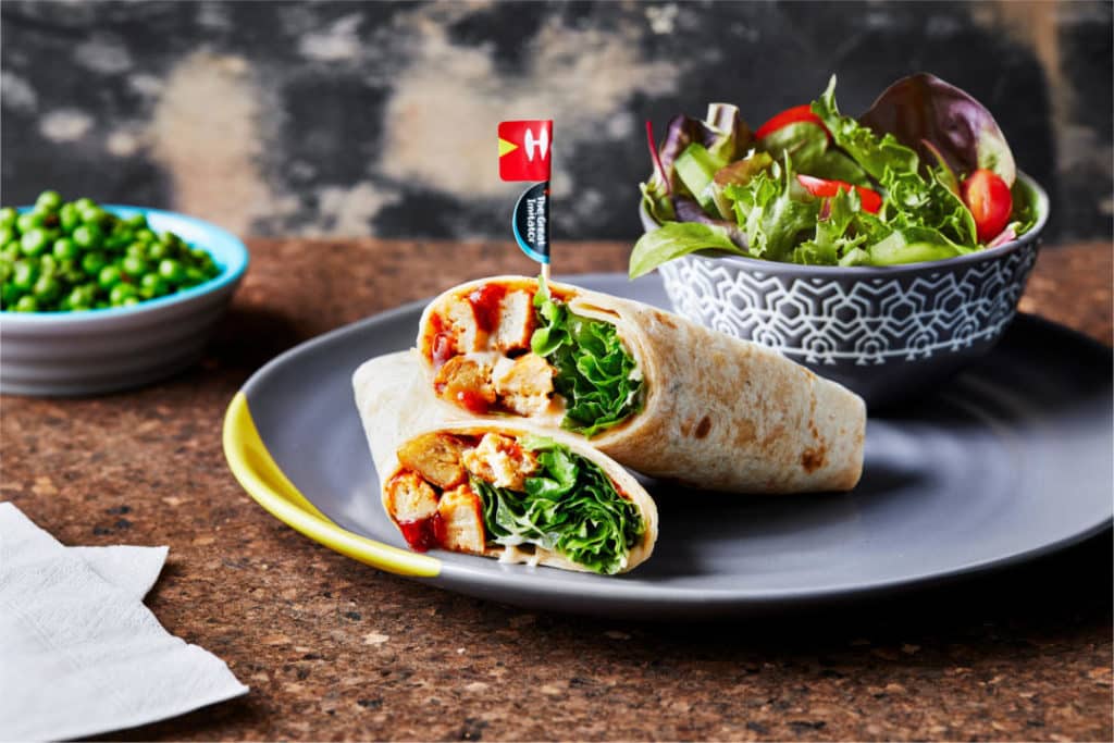 Chicken wrap cut in half on a plate with a side salad and green peas.