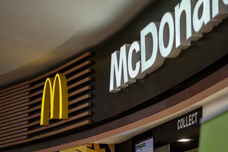 Close-up view of a McDonald's restaurant sign at a motorway service area, featuring the iconic golden arches logo on a dark striped background.